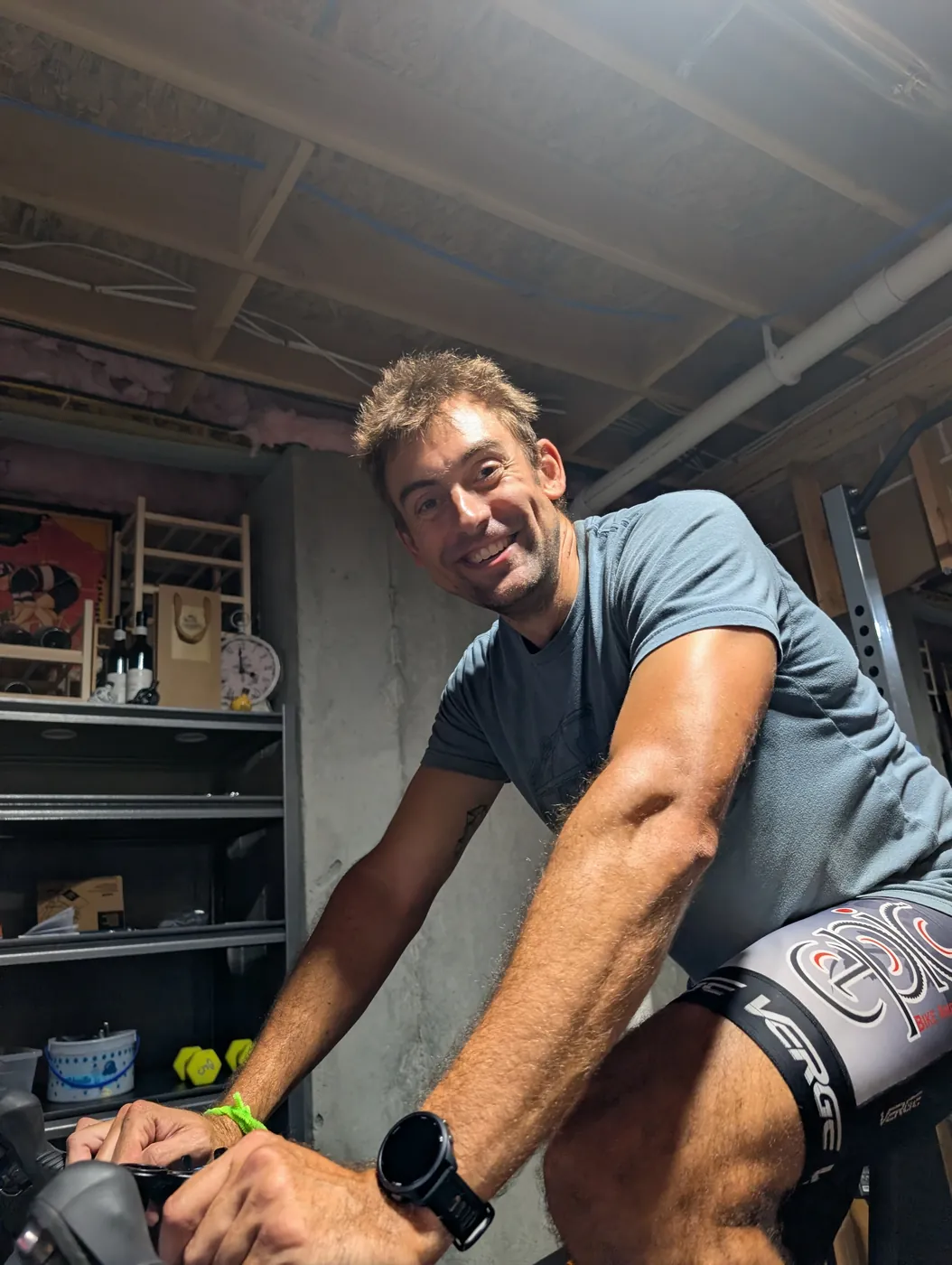 Close, low-angle photo of a man smiling while riding a bike set up on a smart trainer indoors