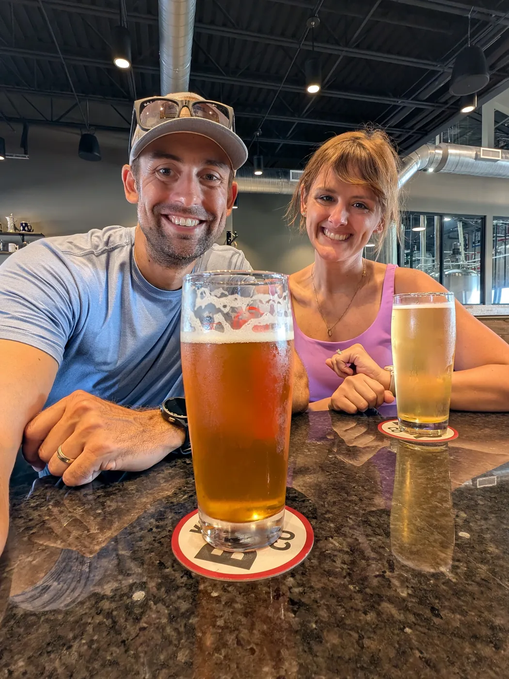 Natalie and me at a brewery bar top with two beers in front of us and the tanks visible through the glass behind