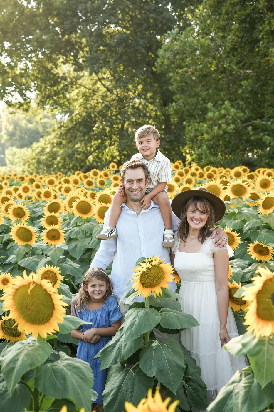 John Rothfusz and his wife Natalie standing in a sunflower field with their two kids, their son up on his shoulders and their daughter in front of them