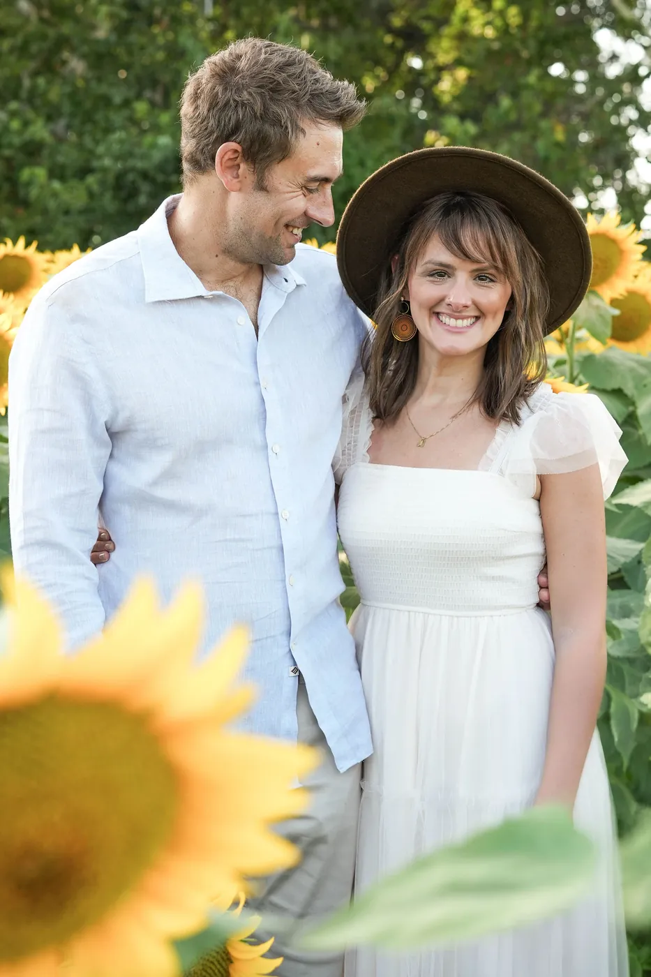 John and Natalie in the sunflowers, his arm around her shoulders, looking over at her while she laughs