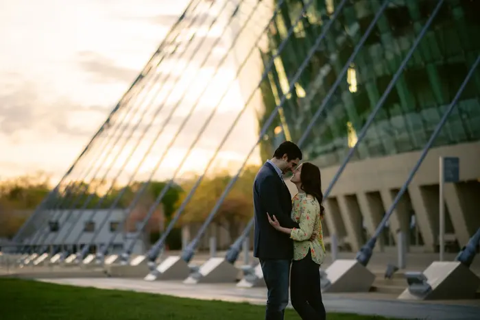 An engaged couple standing forehead to forehead at sunset outside the Kauffman Center for the Performing Arts in Kansas City