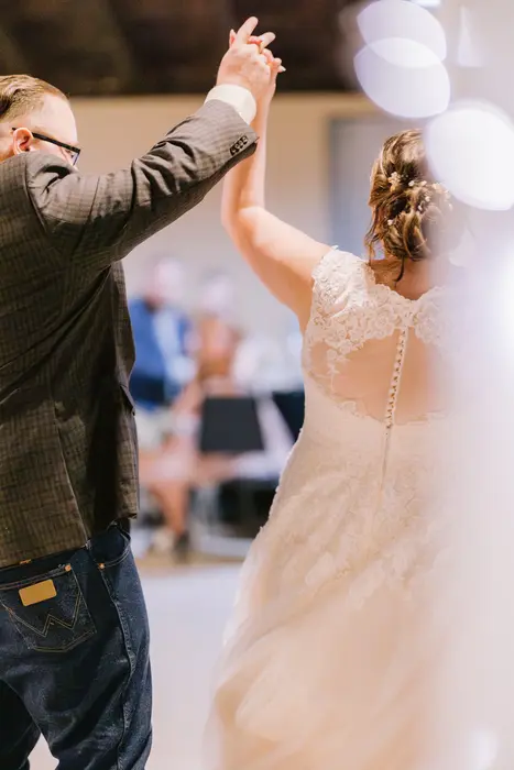 A groom spinning his bride on the dance floor during their first dance, guests watching behind them