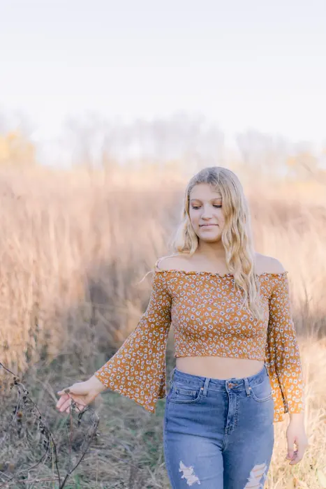 Senior portrait of a young woman walking through tall autumn prairie grass at golden hour