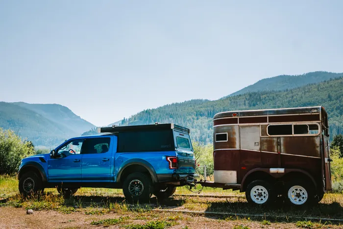 A blue pickup hitched to a weathered vintage trailer, mountains behind